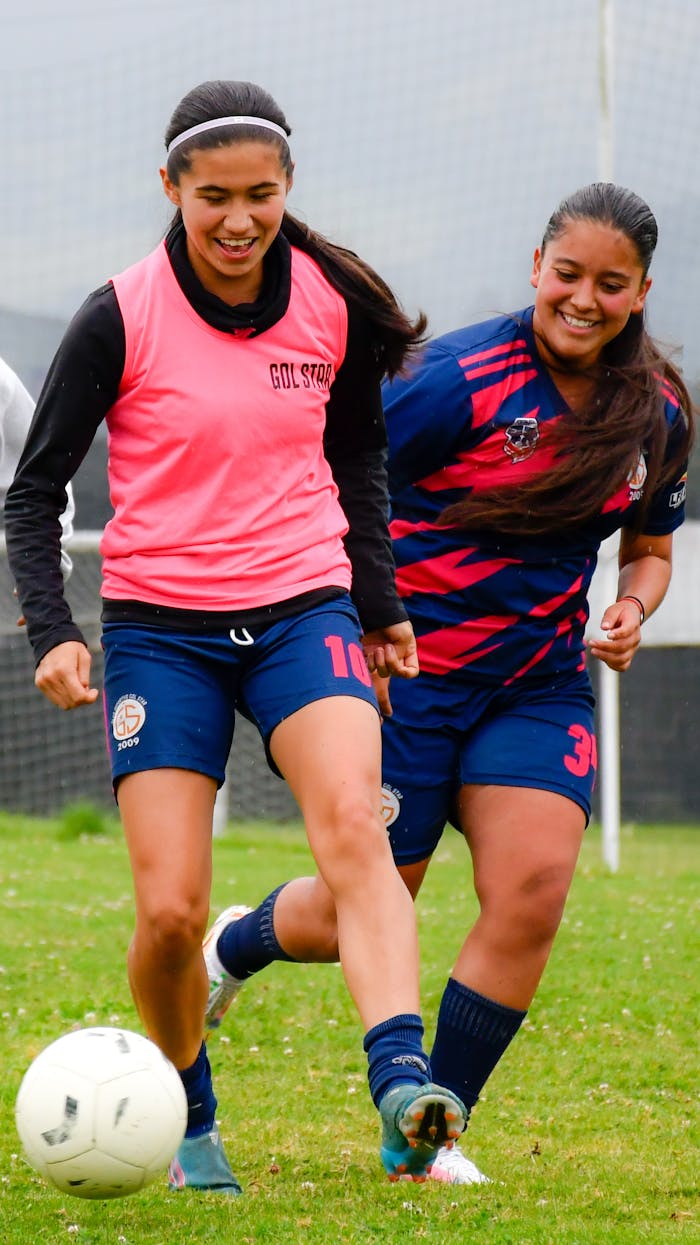 Two teenage girls enjoying an outdoor soccer game, laughing and playing.