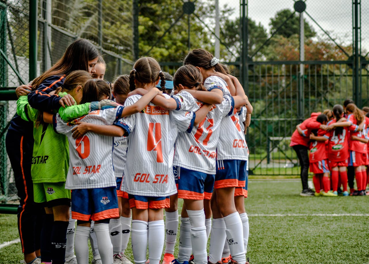 Young soccer team in white uniforms huddling on field, fostering teamwork.